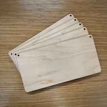 Load image into Gallery viewer, A stack of five blank laser cut rectangular plaques with rounded corners and holes in the top corners, displayed on a wooden surface.