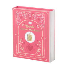 Load image into Gallery viewer, A pink packaging for the Book Locket necklace decorated to look like a real book. With floral embellishments in the corners and "Book Locket Necklace" printed on the cover. The right side edge is designed to look like pages to mimic a real book.