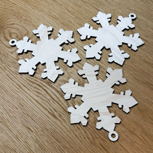Load image into Gallery viewer, Three 3D wooden laser cut snowflakes, each with hanging loops, on a darker wooden surface.