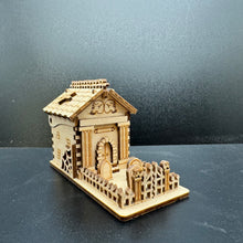 Load image into Gallery viewer, A laser cut model of a Mausoleum. A wonky gate with skulls on the posts fronts the small grave yard. The Mausoleum has layered pillars either side of the front door.
The roof is designed to look like decreped tiles with wooden boards covering gaps. A spikey fence matches the top of the roof.
The back of Mausoleum has a hinge which can open to reveal the centre.