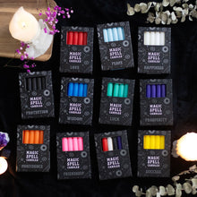 Load image into Gallery viewer, A collection of various boxes of Magic Spell Candles. Items on a black surface with flowers and other lit candles for decoration.