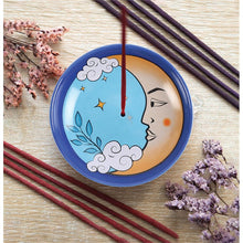 Load image into Gallery viewer, A ceramic incense bowl with a vintage tarot themed moon illustration. The yellow crecent moon has a calm face looking to the centre on a light blue background. Also depicted are white clouds, yellow stars and a blue plant growning from a cloud. The image is framed with a ring of darker blue and the lip or edge of the bowl is lined with a gold like finish. The bowl is resting on a wooden table and a stick of incense it held inside the centre hole. Next to the bowl are sticks of insence and sprigs of flowers.