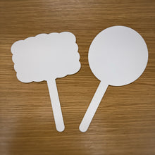Load image into Gallery viewer, Two white laser cut acrylic signs with handles, one rectangular scalloped shaped and one circle shaped sign, placed on a wooden surface.