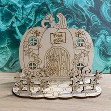 Load image into Gallery viewer, A wooden laser cut fairy house shaped like a pumpkin on a mock stone base with vine styled fencing in front of the house.
On the design features windows, a door, and a sign that reads "Trick or Treat" above the door. The house is flat with no layering but is free-standing on it's base.