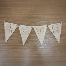 Load image into Gallery viewer, A wooden laser cut scalloped triangular shaped bunting, with a cute font layered on top spelling out "LOVE". Item laid out on a darker wooden surface.
