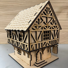 Load image into Gallery viewer, A MDF laser cut Tudor Tavern, with a tiled patterned removable roof, wooden style beam panelling, support beams for the tiered overhanging second floor, a stone stylised door frame and an engraved double sided sign that reads "Ye Olde Book End Inn". The 3D model is to rest a book on the roof to hold your page like a bookmark.