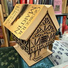 Load image into Gallery viewer, An MDF laser cut Tudor Tavern. with a thick book draped over the roof. It also features wooden style beam panelling, support beams for the tiered overhanging second floor, a stone stylised door frame and an engraved double sided sign that reads "Ye Olde Book End Inn". The 3D model is to rest a book on the roof to hold your page like a bookmark. Item set on a bookshelf. Books are not included in the set.