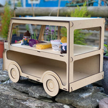 Load image into Gallery viewer, The side and rear of a 3D laser cut food truck cupcake stand made in MDF. Item has knitted gnomes and other items for display and is photographed on a stone wall in a garden. The back and side panels have large openings to store extra cupcakes or other items inside.