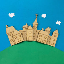 Load image into Gallery viewer, A collection of laser cut toy box village building shapes, layered like a hilltop village against a blue & green background with white clouds.