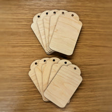 Load image into Gallery viewer, Ten basic laser cut gift tag shapes with a hole at the top, stacked in two piles on top of a wooden background.
