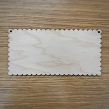Load image into Gallery viewer, A blank laser cut rectangular scalloped plaque with holes in the top corners, displayed on a wooden surface.
