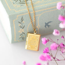 Load image into Gallery viewer, A gold-toned book-shaped pendant necklace with 'You are my favourite chapter' text engraved on the locket's front cover. The gold toned chain hangs over a blue decorative book with pink flowers in the foreground.
