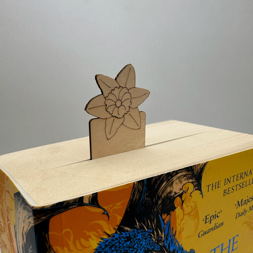 A laser cut bookmark with a daffodil on top, poking out of a thick book.