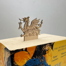 Load image into Gallery viewer, A laser cut bookmark of a Welsh Dragon on top, poking out of a thick book.
