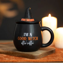 Load image into Gallery viewer, Black mug with witch hat and 'I'm a good witch after coffee' text printed on the front, placed on a wooden surface with candles in the background.
