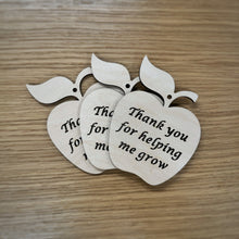 Load image into Gallery viewer, Three laser cut wooden apple shapes with cut out text reading "Thank you for helping me grow" and hole cut out at the top for hanging. Items resting on a darker wood grain surface.
