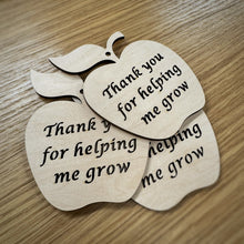 Load image into Gallery viewer, Three laser cut wooden apple shapes with cut out text reading "Thank you for helping me grow" and hole cut out at the top for hanging. Items resting on a darker wood grain surface.
