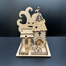 Load image into Gallery viewer, Laser cut halloween themed church model. A spooky tree with a pumpkin style face behind the building. In front is a graveyard garden surrounded by a jagged fence. Cobwebs are scattered in the garden and on the church spire.
