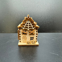 Load image into Gallery viewer, A laser cut haunted house model, face on shot. With boarded up windows and a large cobweb across the peak of the roof. Two tiny pumpkins decorate the front of the house. The front door is shaped like a coffin.
