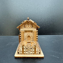 Load image into Gallery viewer, A laser cut model of a Mausoleum from the front. A wonky gate with skulls on the posts fronts the small grave yard. The Mausoleum has layered pillars either side of the front door.
