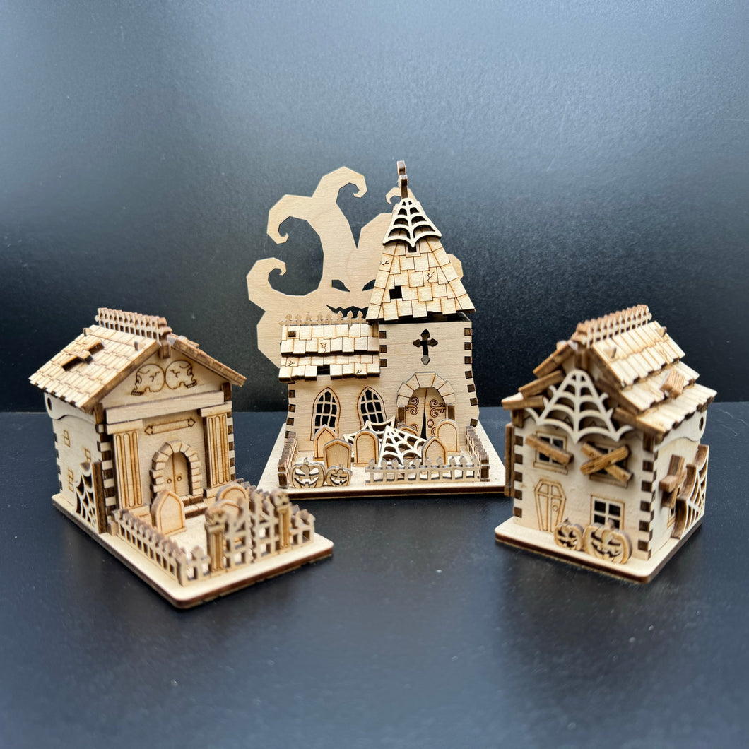 A set of three laser cut models of Halloween buildings. A mausoleum, a church and a house shape.