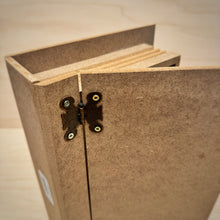 Load image into Gallery viewer, A close up of the metal hinges on a book shaped MDF box. The door of the box is opened slightly and the ribbed edge that emulates pages can be seen.
