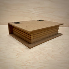 Load image into Gallery viewer, A closed blank book shaped MDF box with working metal hinges and a ribbed side to emulate pages laying flat on a lighter wooden background.
