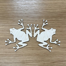 Load image into Gallery viewer, Two wooden laser cut frog shapes on a wood surface.
