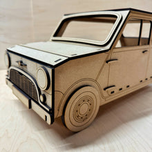 Load image into Gallery viewer, The front corner of a 3D MDF laser cut cupcake stand in the shape of a classic mini car. Item has layered lights, bumpers, grill, logo and other parts. Item on a light wooden background. 
