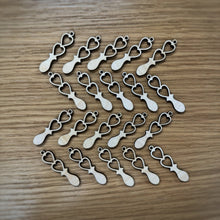 Load image into Gallery viewer, Twenty mini laser cut love spoons. They each have two heart shaped cut outs and a small loop hole at the top. Laid out on a wooden surface.
