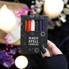 Load image into Gallery viewer, A hand with black nail polish holding a black box of mixed Magic Spell Candles. Some candles in various colours can be seen in the hole of the packaging. Item held over a black surface with candles, crystals and other candles.
