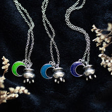 Load image into Gallery viewer, Three necklaces with moon and cauldron pendants on a dark velvet like background and white decorative flowers on the sides of the image. Each crescent moon is a different colour: Green, Blue, &amp; Purple. 
