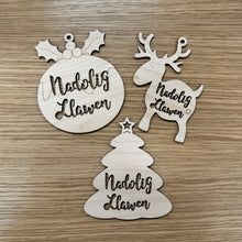Load image into Gallery viewer, Three wooden laser cut baubles in various shapes with the Welsh words: "Nadolig Llawen" cut out from them.
They come in a christmas pudding shape, a reindeer shape, and a christmas tree shape. Items on a wooden background.
