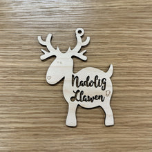 Load image into Gallery viewer, A wooden laser cut reindeer shape with the words "Nadolig Llawen" cut out on the body. Item on a wooden background.
