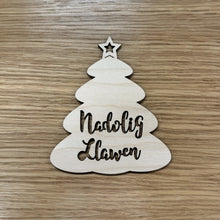 Load image into Gallery viewer, A wooden laser cut Christmas tree shape with the words "Nadolig Llawen" cut out on the body. Item on a wooden background.

