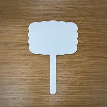 Load image into Gallery viewer, A single white laser cut acrylic sign with a handle, it is rectangular and scalloped shaped, placed on a wooden surface.
