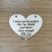 Load image into Gallery viewer, A single heart shaped laser cut plaque, featuring two heart shaped holes at the top for hanging, with the following phrase cut out: "I may not be perfect, but I'm Welsh and that's close enough". A laser cut Welsh Dragon is cut out and layered at the bottom of the heart plaque.
