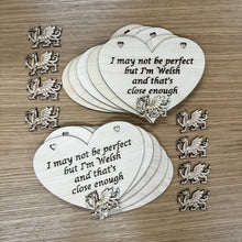 Load image into Gallery viewer, Two stacks of heart shaped laser cut plaques. Featuring two heart shaped holes at the top for hanging, with the following phrase cut out: "I may not be perfect, but I'm Welsh and that's close enough". A space is left at the bottom of the plaques for a laser cut Welsh Dragon to layer at the bottom of the plaque. Both stacks feature a dragon in this space Another eight dragon shapes are positioned next to the plaque stacks to show they're a part of the set.

