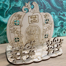 Load image into Gallery viewer, A wooden laser cut fairy house shaped like a pumpkin on a mock stone base with vine styled fencing in front of the house.
On the design features windows, a door, and a sign that reads "Trick or Treat" above the door. The house is flat with no layering but is free-standing on it's base.
