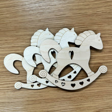 Load image into Gallery viewer, Three wood laser cut rocking horse shapes piled together. Each design has a cut out heart on the body and smaller hearts on the base. Items on a wooden background.
