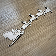 Load image into Gallery viewer, Wooden laser cut of Santa in sleigh with reindeer on a wooden surface
