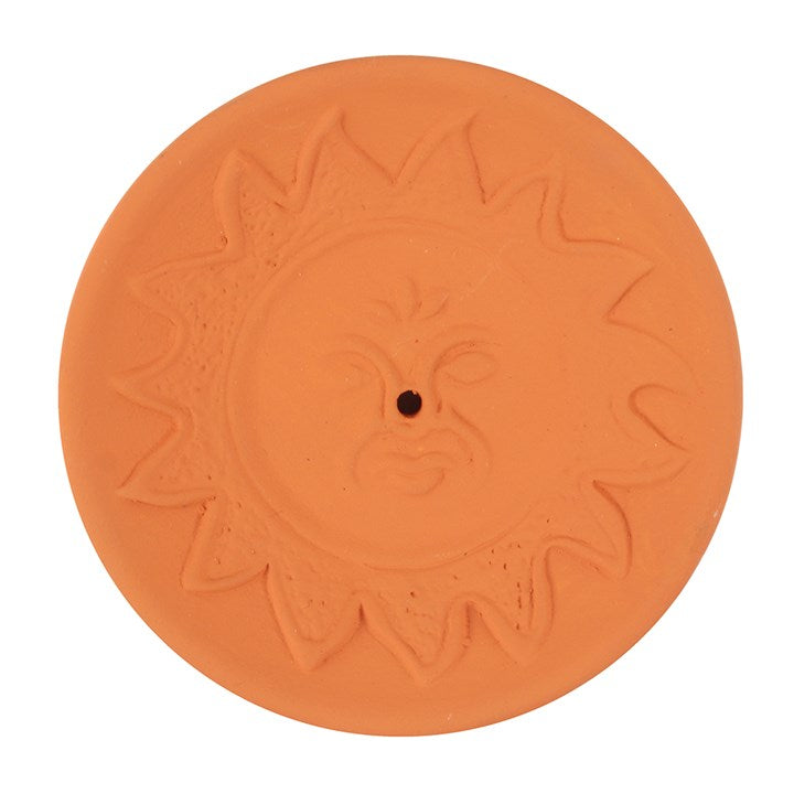 A terracotta incense stick holder plate with an embossed sun and face design.