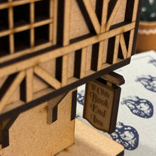 Load image into Gallery viewer, A close-up of a laser cut wooden model of a Tudor style tavern with mock hanging sign reading "Ye Olde Book End Inn", set on a table of books.
