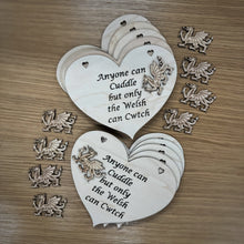 Load image into Gallery viewer, Ten laser cut heart shaped plaques with the phrase "Anyone can Cuddle but only the Welsh can Cwtch" cut out of the hearts and ten layered, unattached Welsh Dragon shapes to glue onto the plaques. Items on a wooden background.
