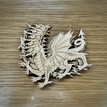 Load image into Gallery viewer, A stack of five laser-cut Welsh dragon shapes in a light natural maple wood finish, arranged on a darker wood-grain surface.
