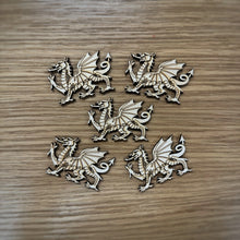 Load image into Gallery viewer, Five small laser-cut Welsh dragon shapes in a light natural maple wood finish, arranged on a darker wood-grain surface.
