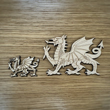 Load image into Gallery viewer, Two wooden laser cut Welsh Dragon shapes in two sizes available. One in 6cm long and another 12cm long. Both on a wooden surface.
