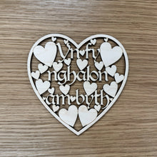 Load image into Gallery viewer, Heart-shaped wooden plaque with cut out text reading: "Yn fy Nghalon am byth". Which translates from Welsh to: "In my heart forever". Smaller hearts suspend the text within a heart shaped border frame.
Item on a wooden surface. 

