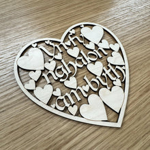 Load image into Gallery viewer, Heart-shaped wooden plaque with cut out text reading: "Yn fy Nghalon am byth". Which translates from Welsh to: "In my heart forever". Smaller hearts suspend the text within a heart shaped border frame. Photograph taken at angle and item is placed on a wooden surface.
