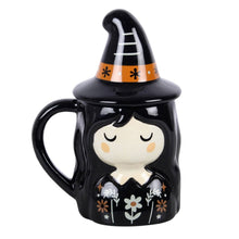 Load image into Gallery viewer, Halloween-themed mug with witch design and black hat lid on top. Item has closed eyes and rosy cheeks, black hair framing a pale head and neck. On the mug's dress design are orange and white floral patterns. The hat lid has an orange stripe and white fold marks. The handle juts out on the left of the mug facing the camera.
Item on a white background.
